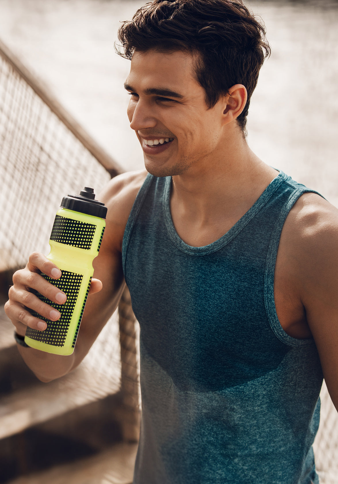 Man in a blue tank top holding a yellow water bottle outdoors