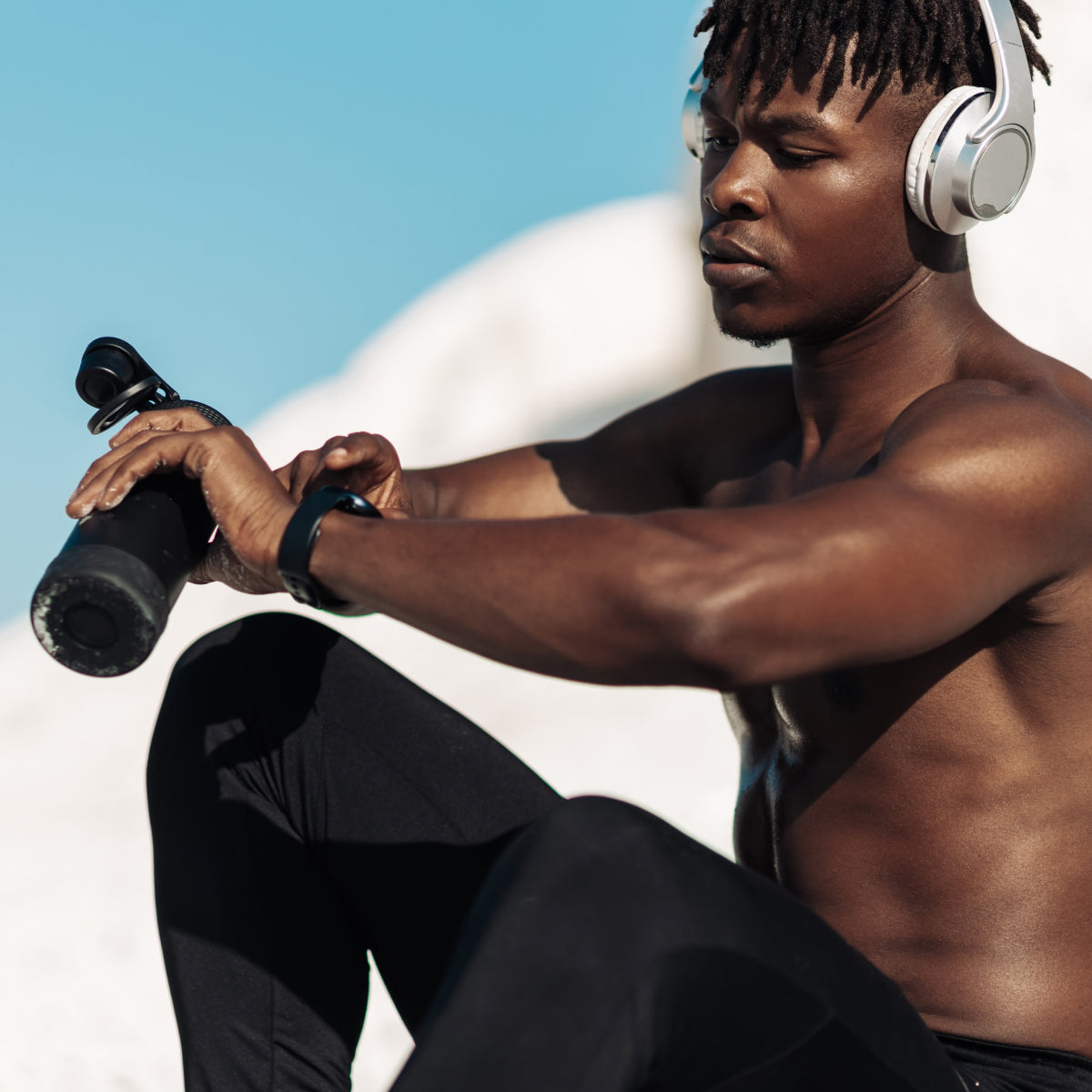 Man exercising outdoors with a dumbbell and headphones on a clear day looking at a smartwatch