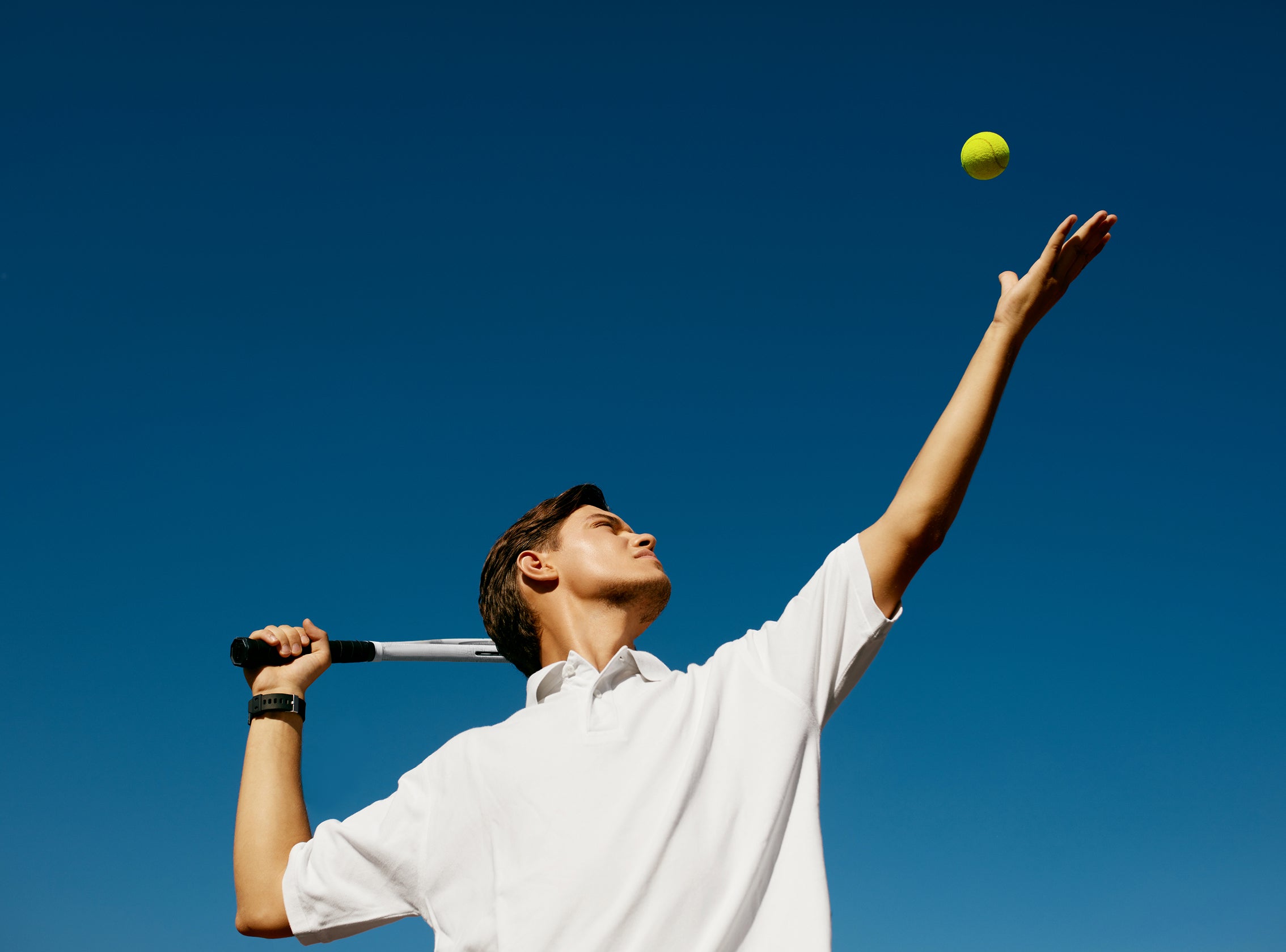 Person preparing to hit a tennis ball against a clear blue sky